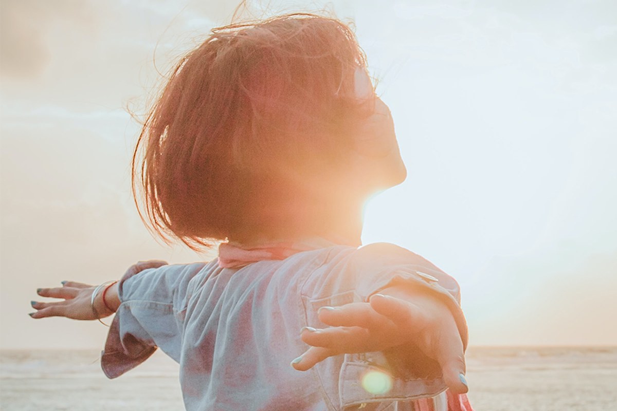 Respirare con il Respiro Originario® Donna di spalle a braccia aperte davanti al mare al tramonto, mentre respira nella luce del sole