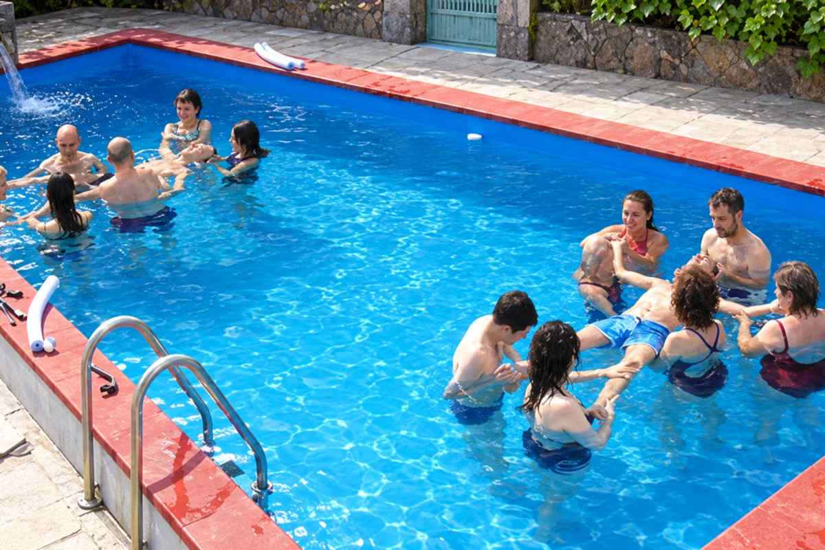 Coccoloterapia® – Esperienza di gruppo in piscina Due gruppi di adulti sostengono persone distese in galleggiamento in una piscina all’aperto